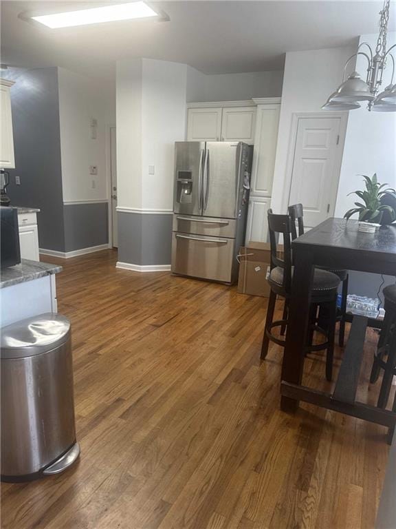 kitchen featuring dark stone counters, white cabinets, stainless steel fridge with ice dispenser, dark wood-type flooring, and pendant lighting