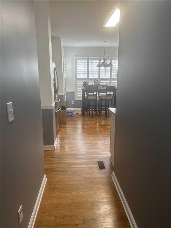 corridor with baseboards, visible vents, an inviting chandelier, and wood finished floors