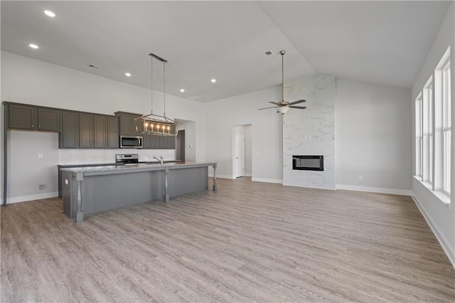 kitchen with an island with sink, high vaulted ceiling, stainless steel appliances, light hardwood / wood-style flooring, and decorative light fixtures