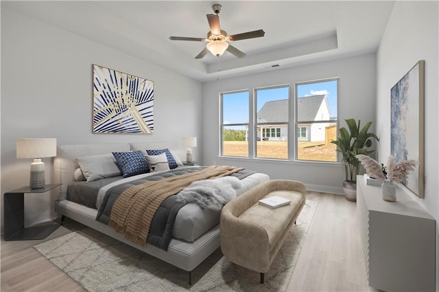 bedroom with light wood-type flooring, ceiling fan, and a tray ceiling