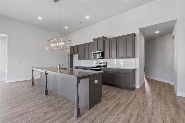 kitchen with an island with sink, hardwood / wood-style floors, a breakfast bar, hanging light fixtures, and appliances with stainless steel finishes