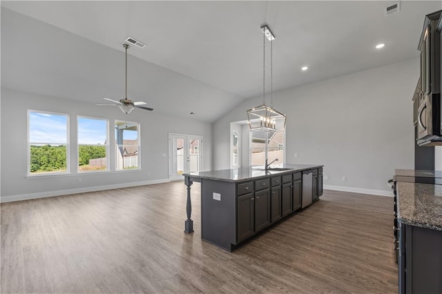 kitchen with dark hardwood / wood-style floors, pendant lighting, dark stone counters, vaulted ceiling, and a center island with sink