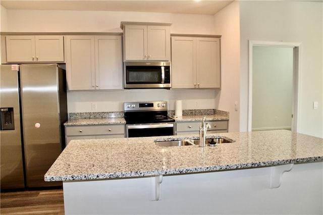 kitchen featuring stainless steel appliances, sink, light stone counters, a kitchen bar, and dark wood-type flooring