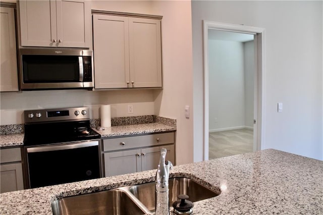 kitchen with gray cabinetry, light stone countertops, appliances with stainless steel finishes, and sink