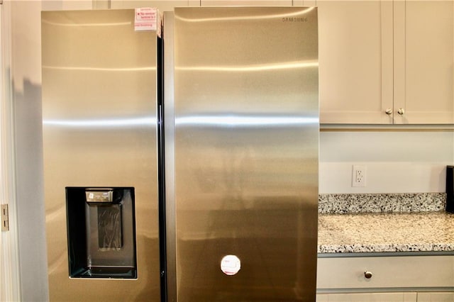 interior details with light stone countertops, stainless steel refrigerator with ice dispenser, and white cabinets