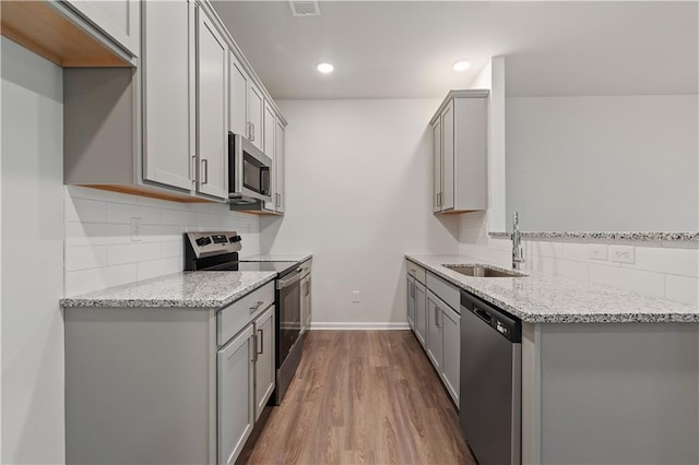 kitchen with appliances with stainless steel finishes, light stone counters, gray cabinetry, sink, and hardwood / wood-style flooring