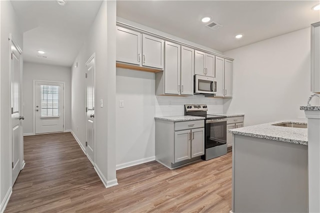 kitchen with light stone countertops, appliances with stainless steel finishes, light wood-type flooring, sink, and gray cabinets