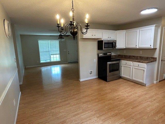 kitchen featuring appliances with stainless steel finishes, a chandelier, dark countertops, light wood-style flooring, and white cabinetry