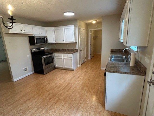 176 Elbert St, Chatsworth, GA 30705 - kitchen with appliances with stainless steel finishes, dark countertops, a sink, white cabinetry, and baseboards