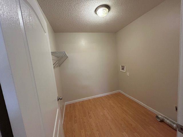 laundry area with washer hookup, light wood finished floors, a textured ceiling, and baseboards