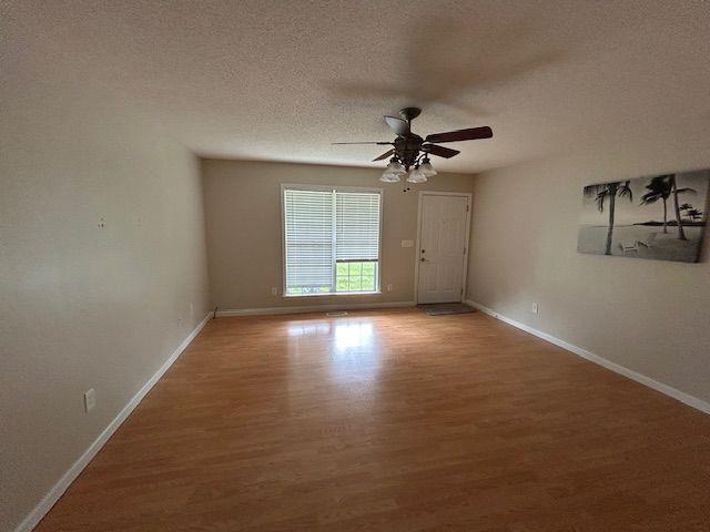 unfurnished room featuring wood finished floors, baseboards, ceiling fan, and a textured ceiling