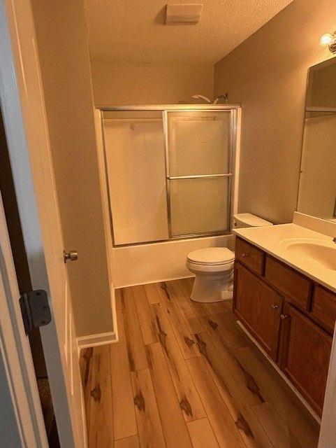 176 Elbert St, Chatsworth, GA 30705 - bathroom featuring a textured ceiling, wood finished floors, toilet, vanity, and bath / shower combo with glass door