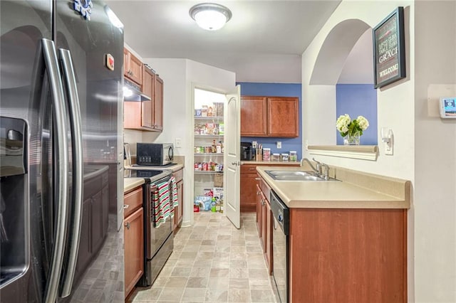 kitchen featuring a sink, brown cabinetry, under cabinet range hood, and stainless steel appliances