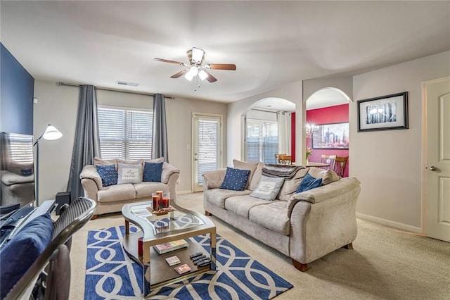 carpeted living area featuring plenty of natural light, arched walkways, visible vents, and baseboards