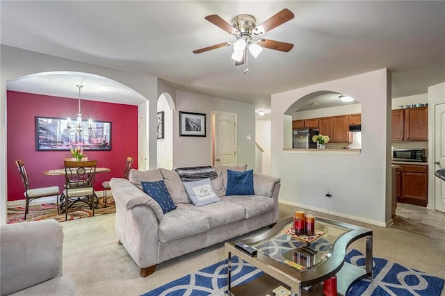 living room with baseboards, light colored carpet, arched walkways, and ceiling fan with notable chandelier