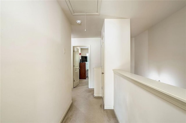 corridor featuring light colored carpet, attic access, and baseboards