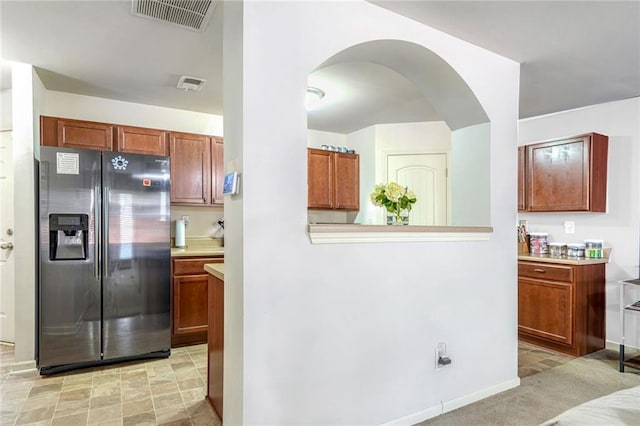 kitchen featuring brown cabinetry, visible vents, light countertops, and stainless steel fridge with ice dispenser