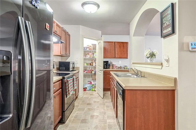 kitchen featuring under cabinet range hood, stainless steel appliances, brown cabinetry, and a sink