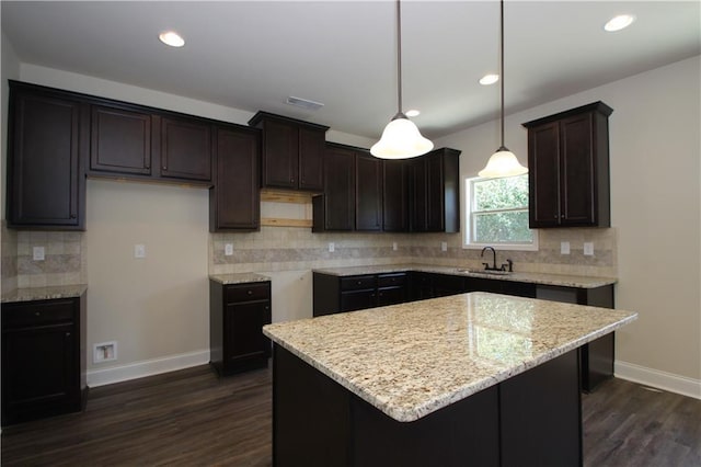 kitchen featuring a center island, dark wood-type flooring, sink, light stone countertops, and decorative light fixtures