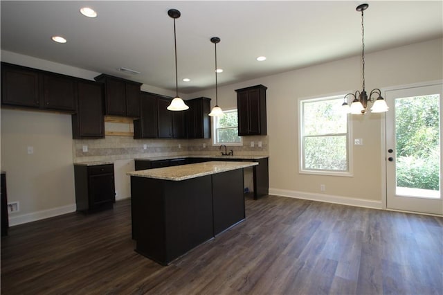 kitchen with dark wood-type flooring, an inviting chandelier, hanging light fixtures, tasteful backsplash, and a kitchen island