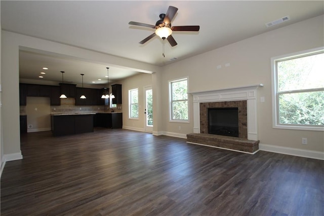 unfurnished living room featuring a fireplace, ceiling fan with notable chandelier, and dark hardwood / wood-style floors