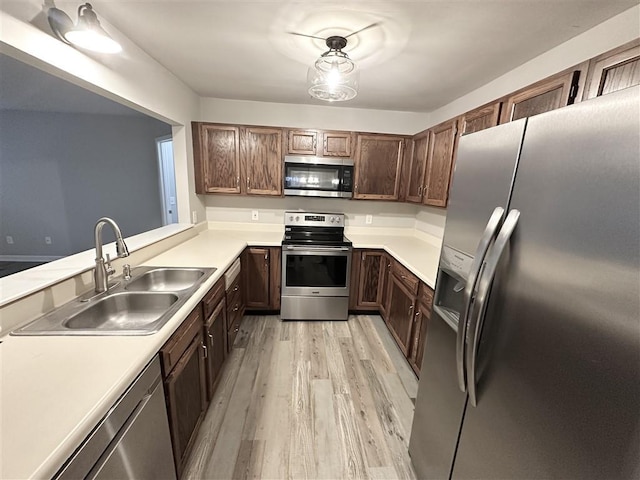 kitchen with kitchen peninsula, appliances with stainless steel finishes, dark brown cabinets, sink, and light hardwood / wood-style flooring