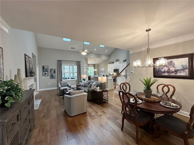 dining area with vaulted ceiling with skylight, dark wood finished floors, stairway, baseboards, and ceiling fan with notable chandelier