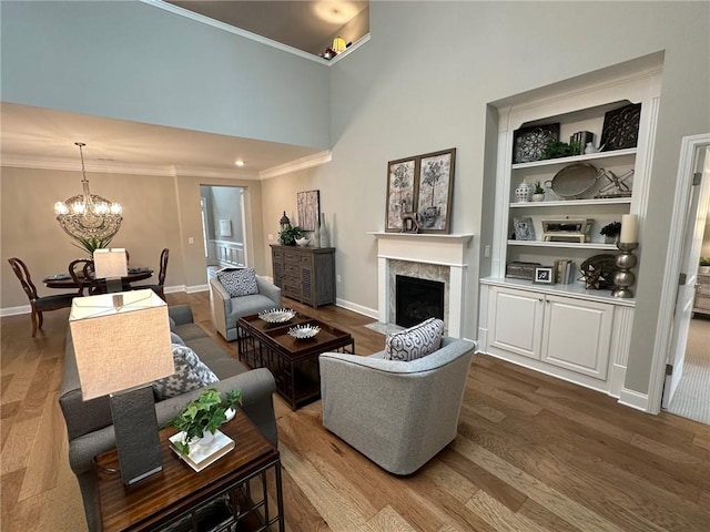 living room featuring a towering ceiling, wood finished floors, baseboards, a chandelier, and a fireplace with flush hearth