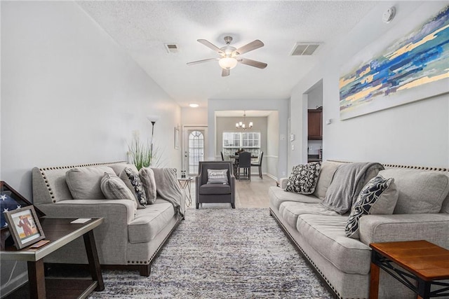 living area with a textured ceiling, visible vents, wood finished floors, and ceiling fan with notable chandelier