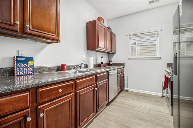 kitchen featuring light wood-style flooring, a sink, baseboards, appliances with stainless steel finishes, and dark countertops