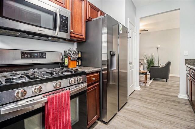 kitchen featuring stainless steel appliances, dark countertops, light wood-style flooring, dark brown cabinets, and baseboards