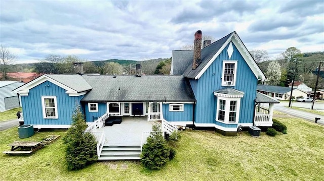 back of property with a chimney, board and batten siding, a yard, and a wooden deck