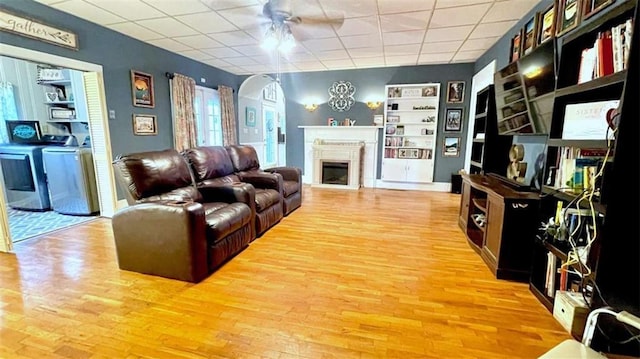 living area featuring arched walkways, light wood-style floors, a ceiling fan, a drop ceiling, and built in features