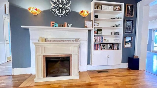 living room with wood finished floors, a glass covered fireplace, and a chandelier