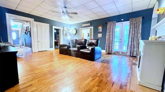 living area featuring wood finished floors, a drop ceiling, a ceiling fan, and baseboards