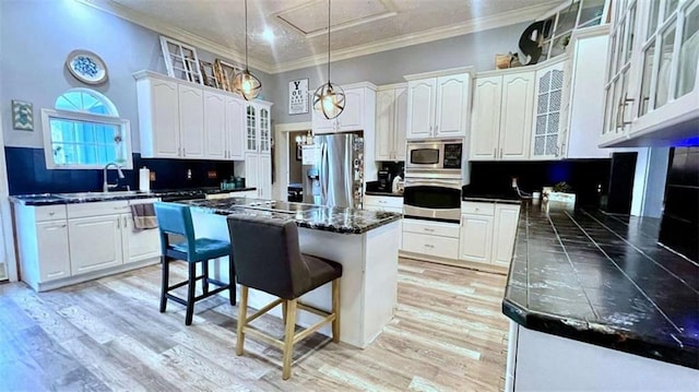 kitchen with stainless steel appliances, dark countertops, a kitchen bar, a sink, and white cabinets