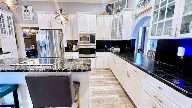 kitchen featuring appliances with stainless steel finishes, white cabinets, a breakfast bar area, decorative light fixtures, and crown molding