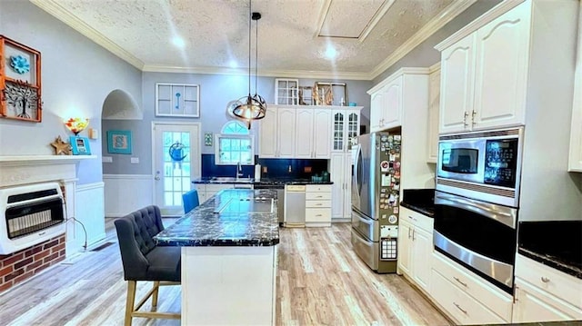 kitchen with stainless steel appliances, heating unit, dark countertops, a kitchen breakfast bar, and light wood-style flooring