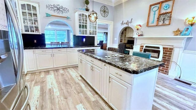 kitchen with freestanding refrigerator, black electric stovetop, a brick fireplace, dark countertops, and arched walkways