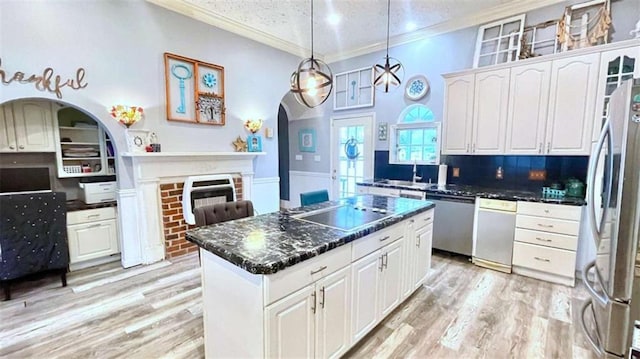 kitchen with appliances with stainless steel finishes, ornamental molding, arched walkways, white cabinetry, and a fireplace