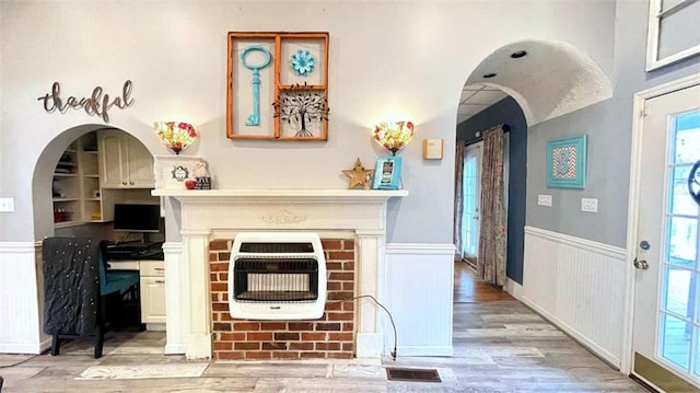living area with heating unit, wainscoting, light wood-type flooring, and healthy amount of natural light