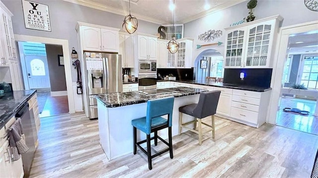 kitchen with appliances with stainless steel finishes, crown molding, a kitchen bar, arched walkways, and glass insert cabinets