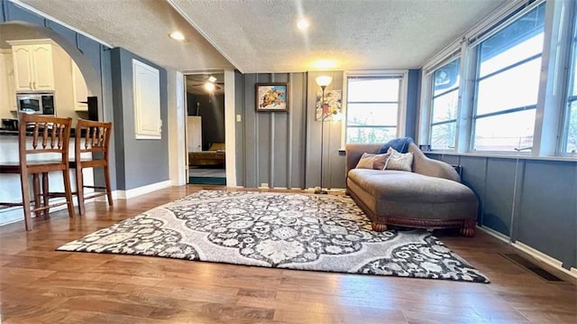 living area featuring a textured ceiling, arched walkways, wood finished floors, baseboards, and recessed lighting