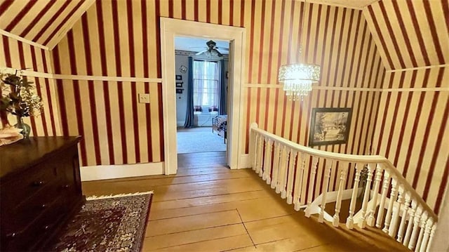 corridor with wallpapered walls, hardwood / wood-style flooring, vaulted ceiling, and a chandelier
