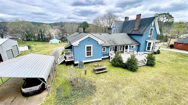 back of house featuring a chimney, a yard, concrete driveway, and a carport