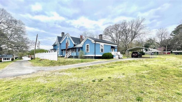 view of side of property featuring driveway, a carport, a lawn, and a chimney