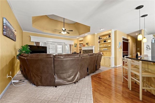 living area with ceiling fan, a fireplace, baseboards, a raised ceiling, and crown molding