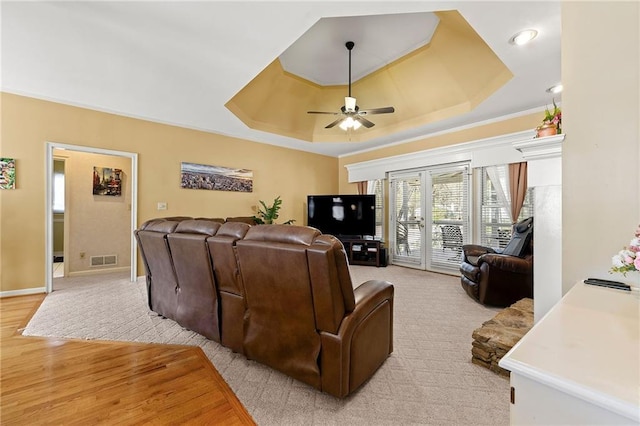 living room with a raised ceiling, visible vents, a ceiling fan, light wood-type flooring, and baseboards