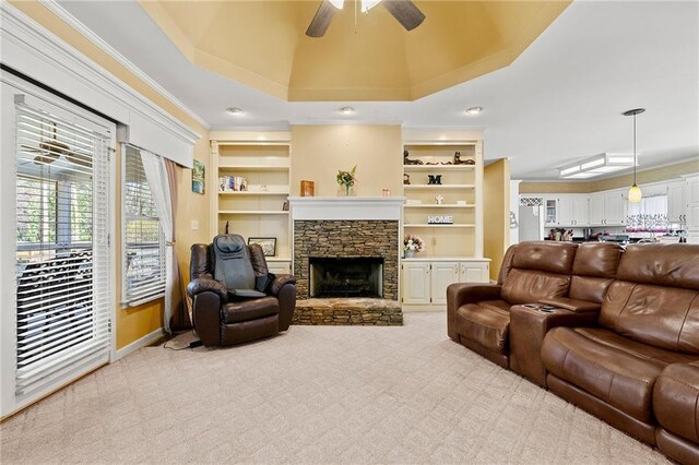 carpeted living area with a stone fireplace, ornamental molding, a ceiling fan, and built in features