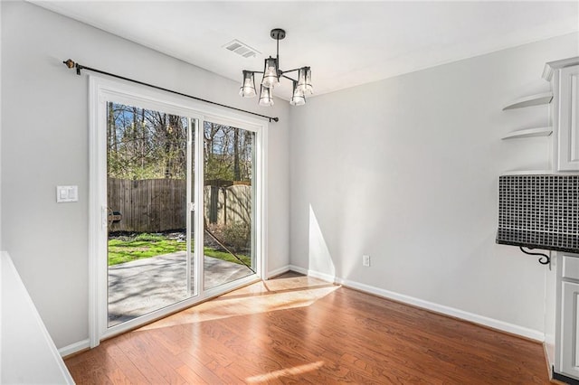 unfurnished dining area featuring a notable chandelier, visible vents, baseboards, and wood finished floors